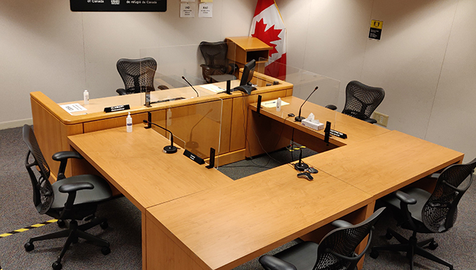 Inside a public hearing room on the 18th floor, there is a round table set up with the public seating blocked off, hand sanitizer and plexiglass installed on tables, along with new health and safety signs on the floor and walls.